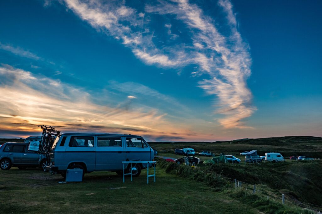 A campervan parked in a campsite in the foreground with other cars and tents in the background