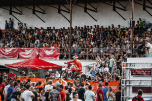An Enduro GP rider is mid air over a jump at the Slovakia Enduro GP event. There are crowd either side of the track.